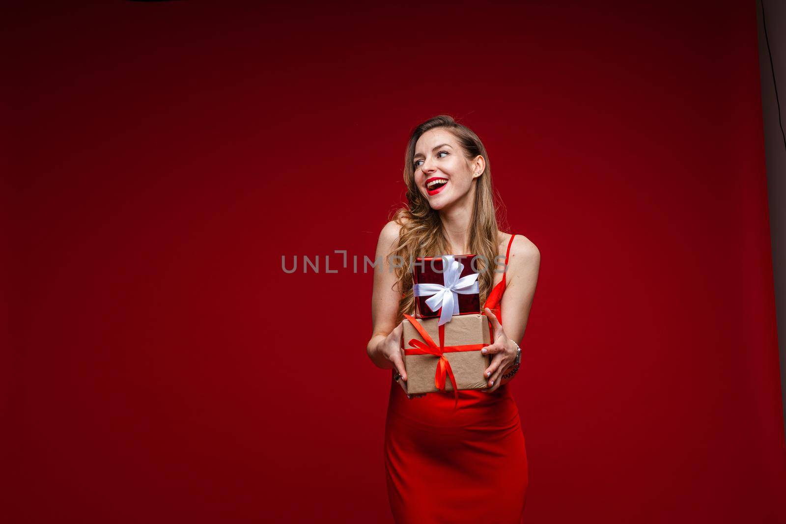 beautiful female fashion model in red dress holds a lot of small boxes with presents by StudioLucky