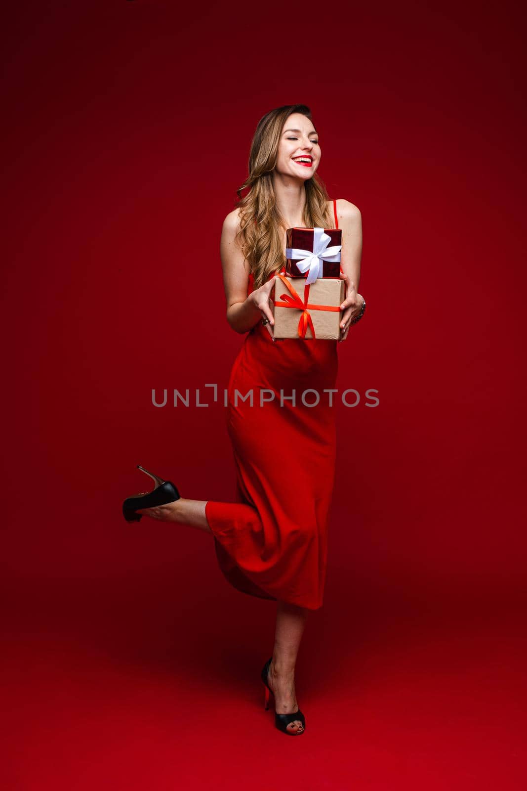 Full length of smiling pretty woman posing and holding gift boxes, isolated on red background. Saint Valentine Day concept