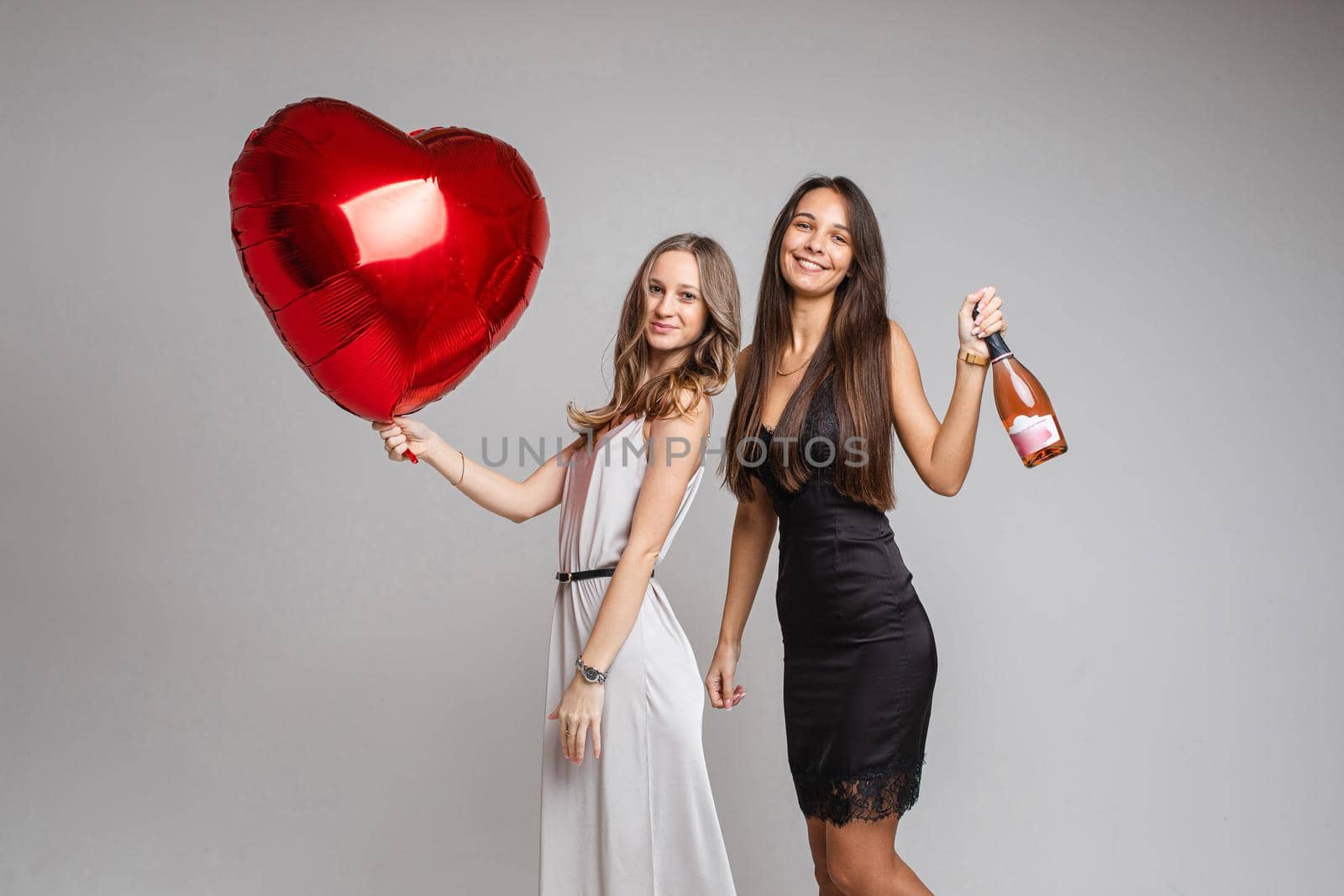 beautiful female friends in dresses with champagne and a big red baloon, isolated on white background
