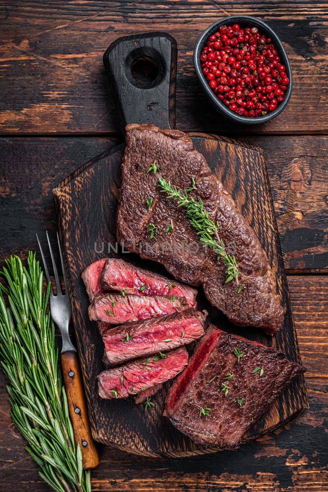 Grilled sliced skirt beef meat steak on a cutting board with herbs. Dark wooden background. Top view by Composter