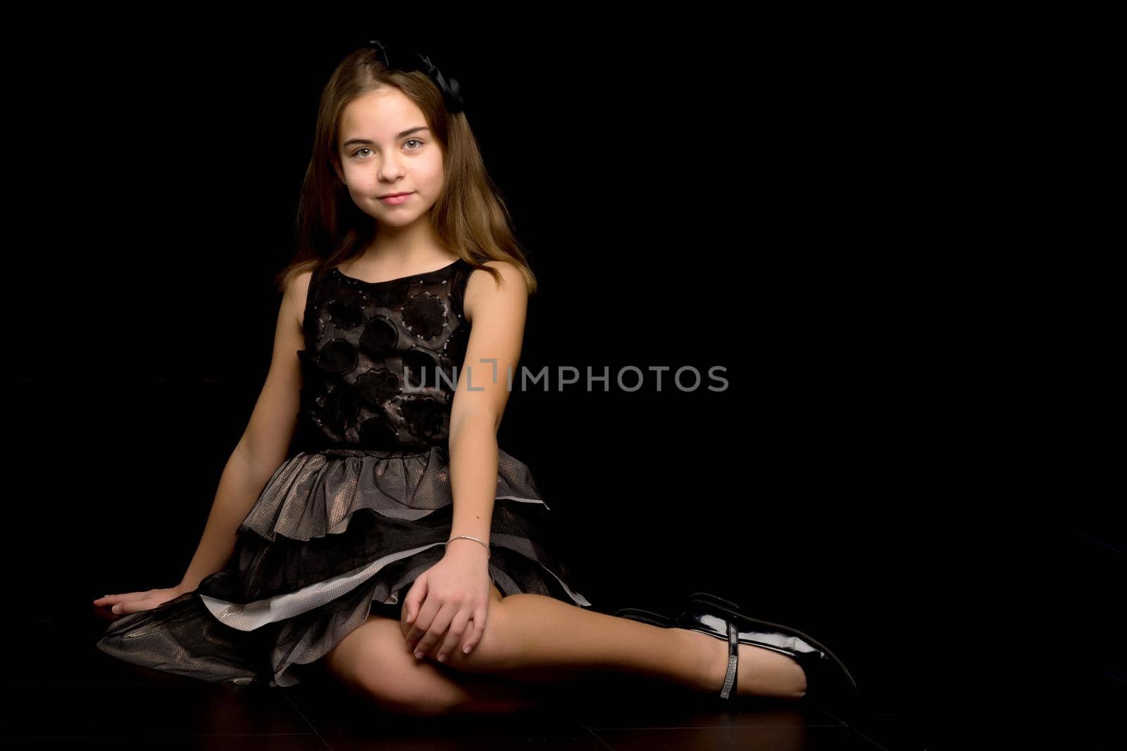 Beautiful little girl sitting in the studio on the floor on a black background. The concept of style and fashion.