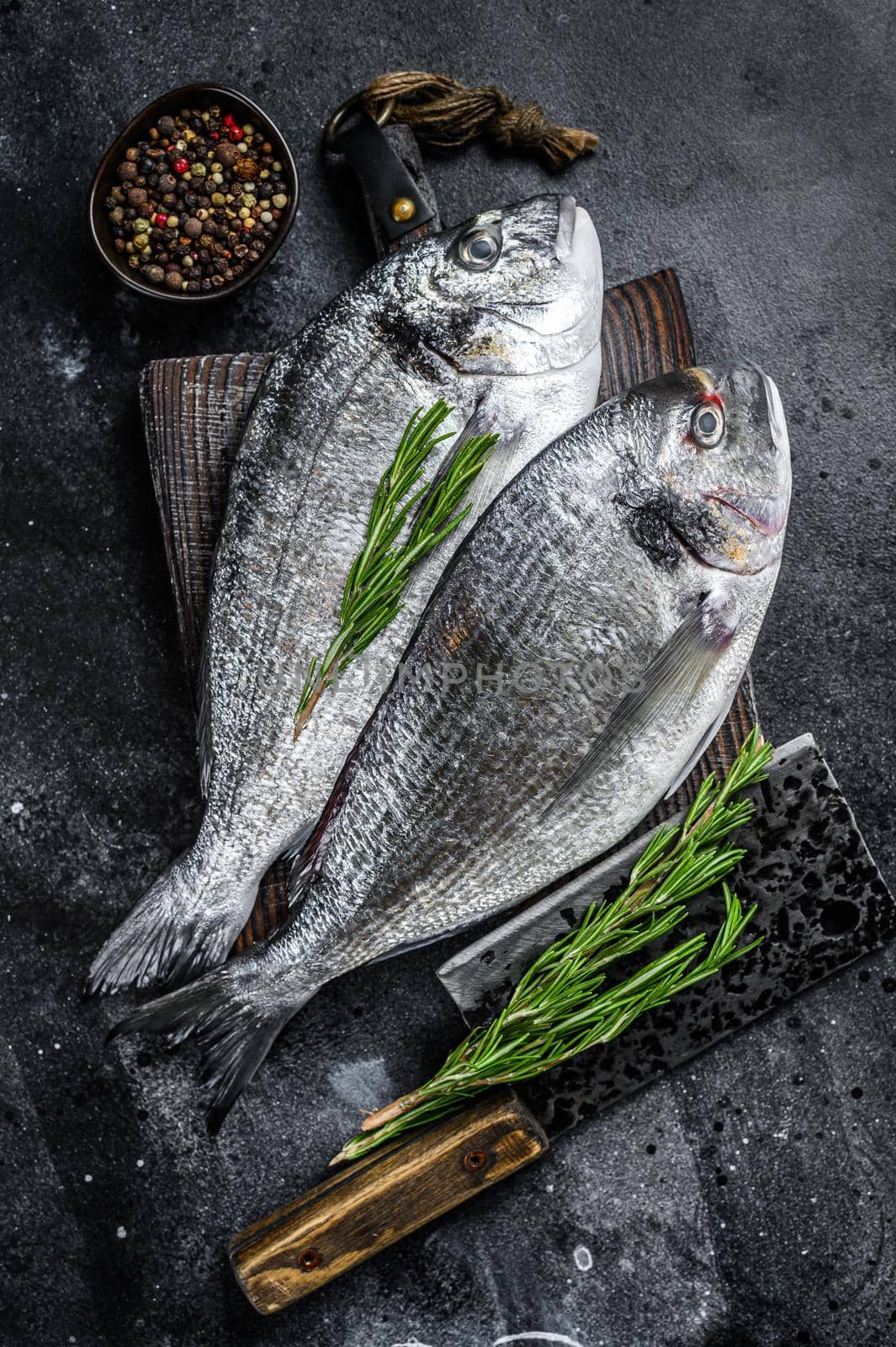 Raw Sea bream dorado fish on a cutting board. Black background. Top view by Composter
