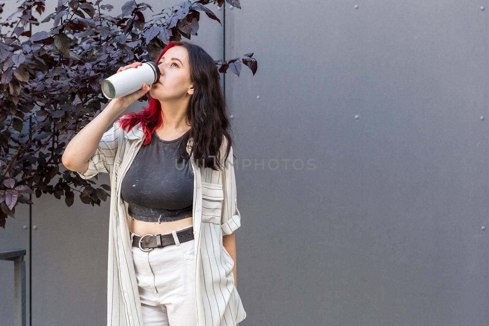 Young woman drinking from the reusable insulated mug. Stay hydrated concept