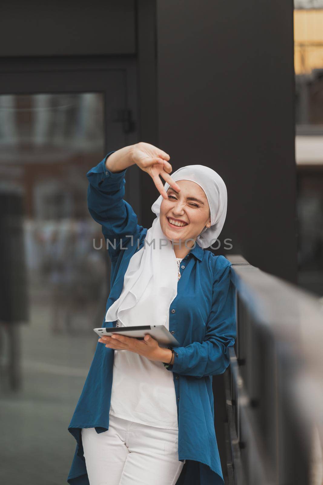 Portrait of an Arab student girl holding a tablet. Arab business woman in hijab holding a tablet in the street. Woman is dressed in hijab.
