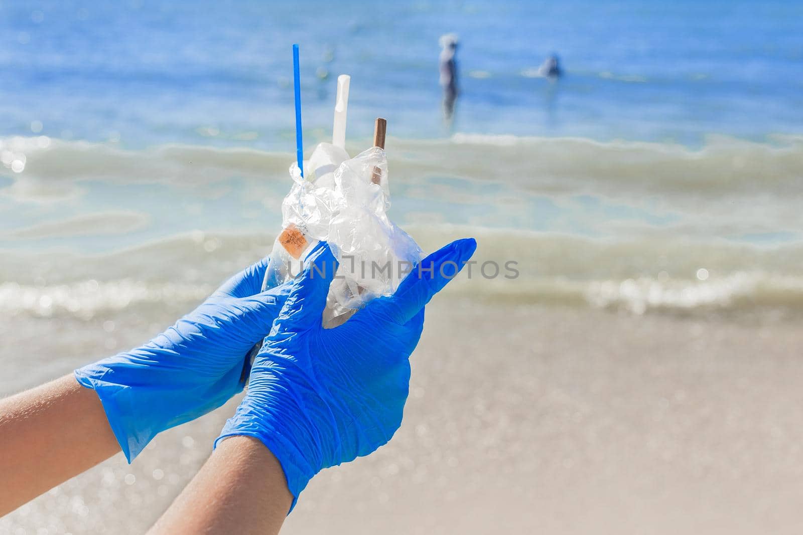 Hands in blue protective household gloves hold a pile of garbage in a bag against the sea. Waste disposal.