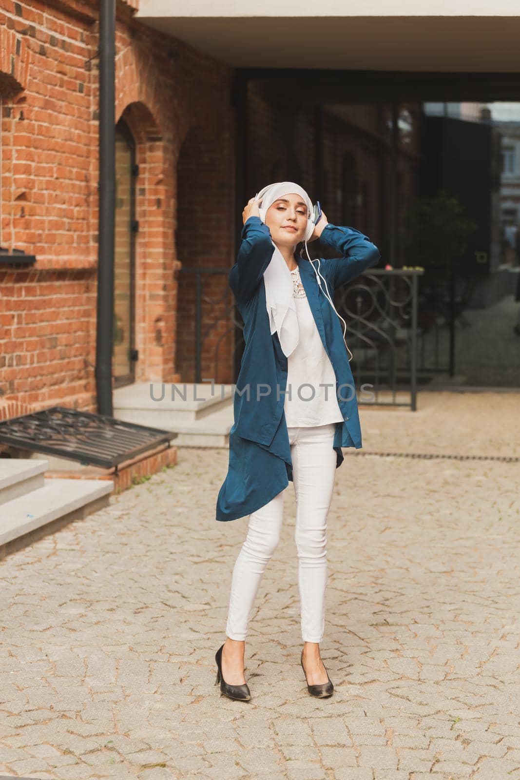 Portrait of young modern arabian woman holding mobile phone and listening the music to headphone