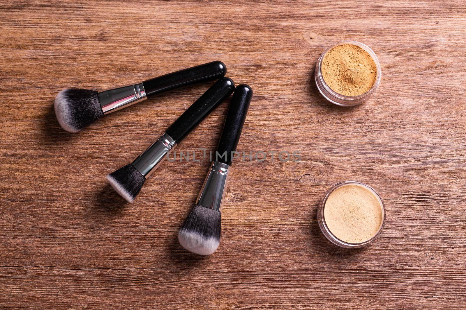 Loose compact mineral powder for face and a brushes for powder and visage on wooden background. Eco friendly and organic cosmetics