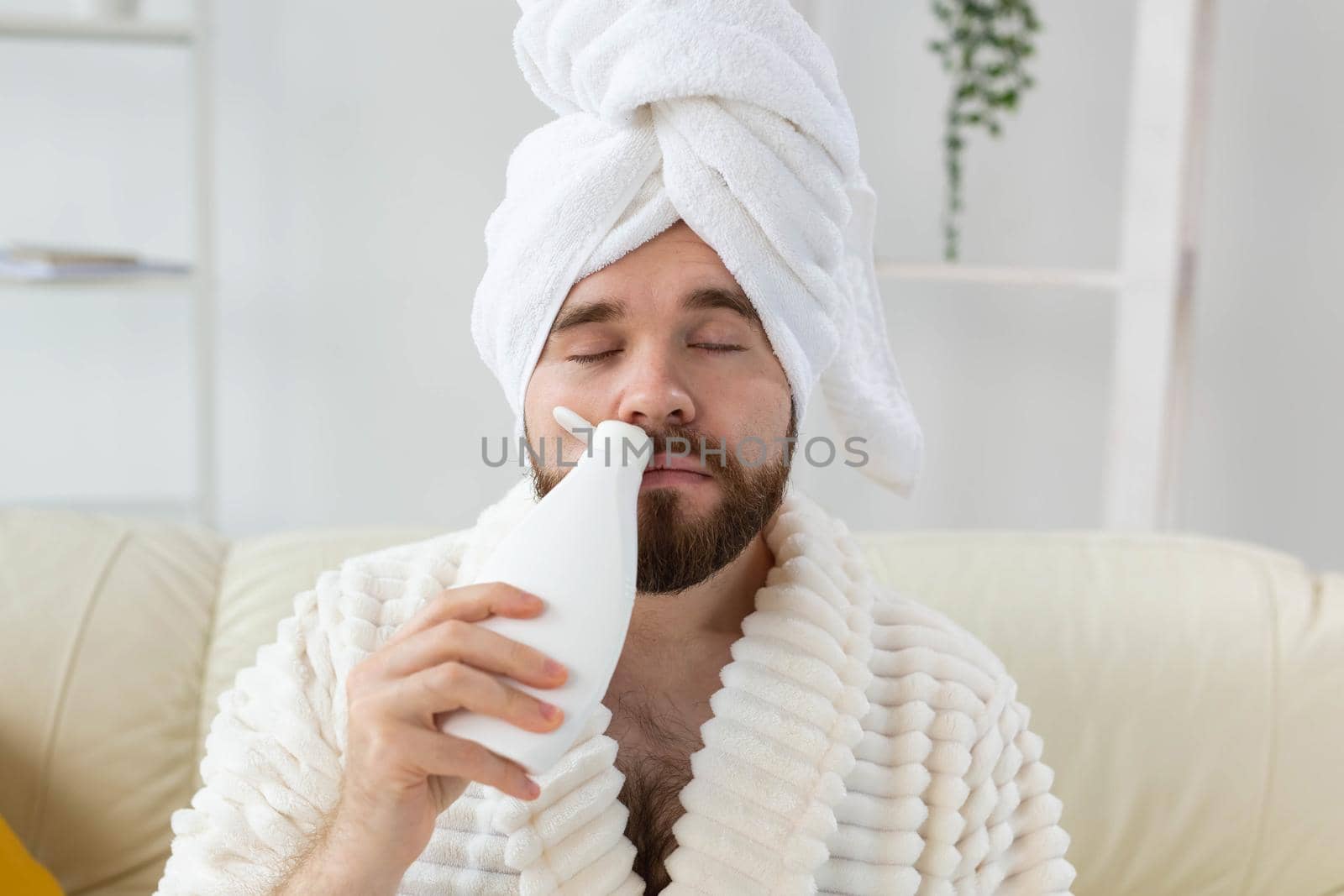 Bearded male with towel on his head applying body lotion cream. Guy smile when smell lotion cream on hand. Spa, body and skin care for man concept.