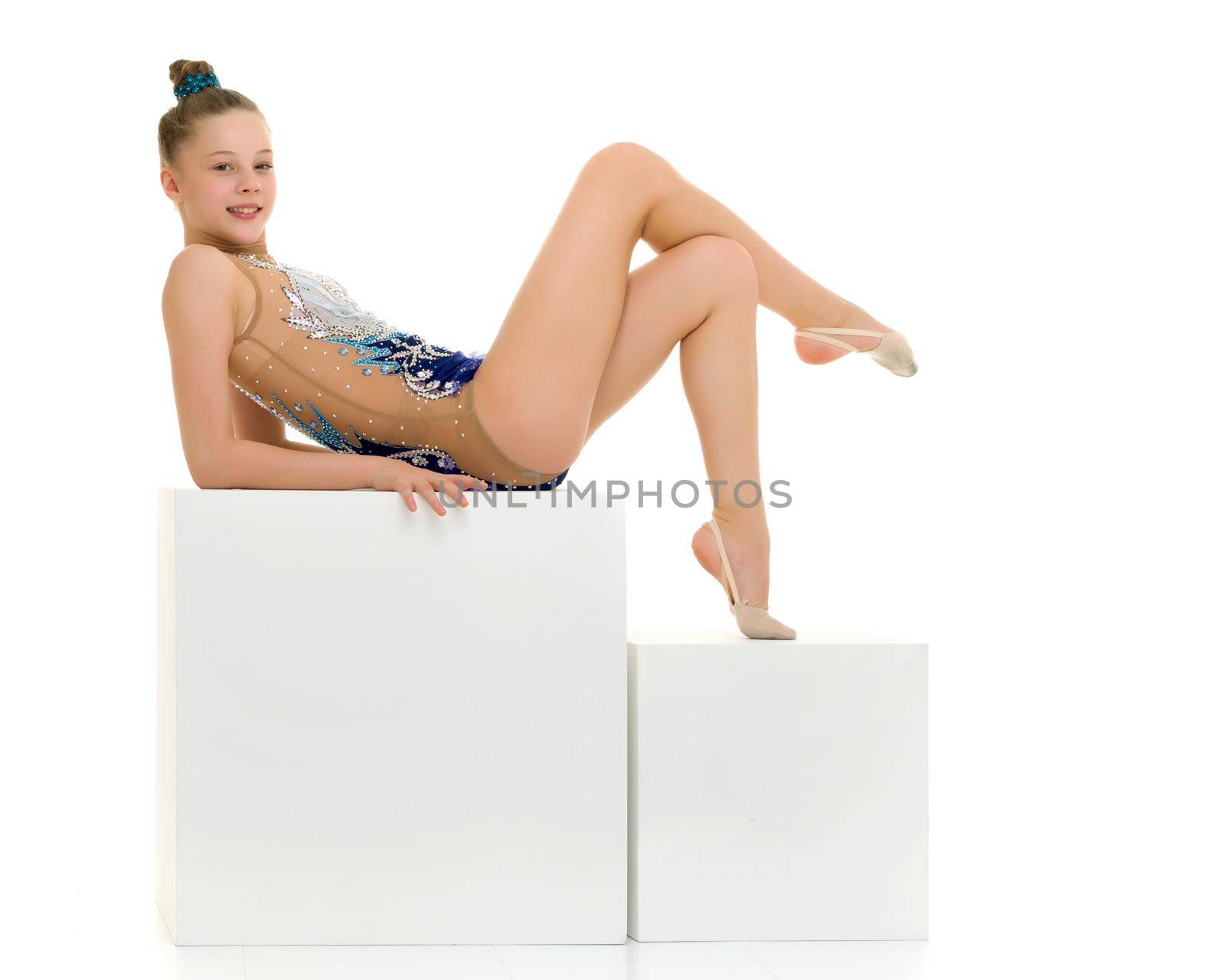 Elegant little gymnast girl in a beautiful sports swimsuit, on the Big White Cube in the studio performs a gymnastic element. Separately on a white background.