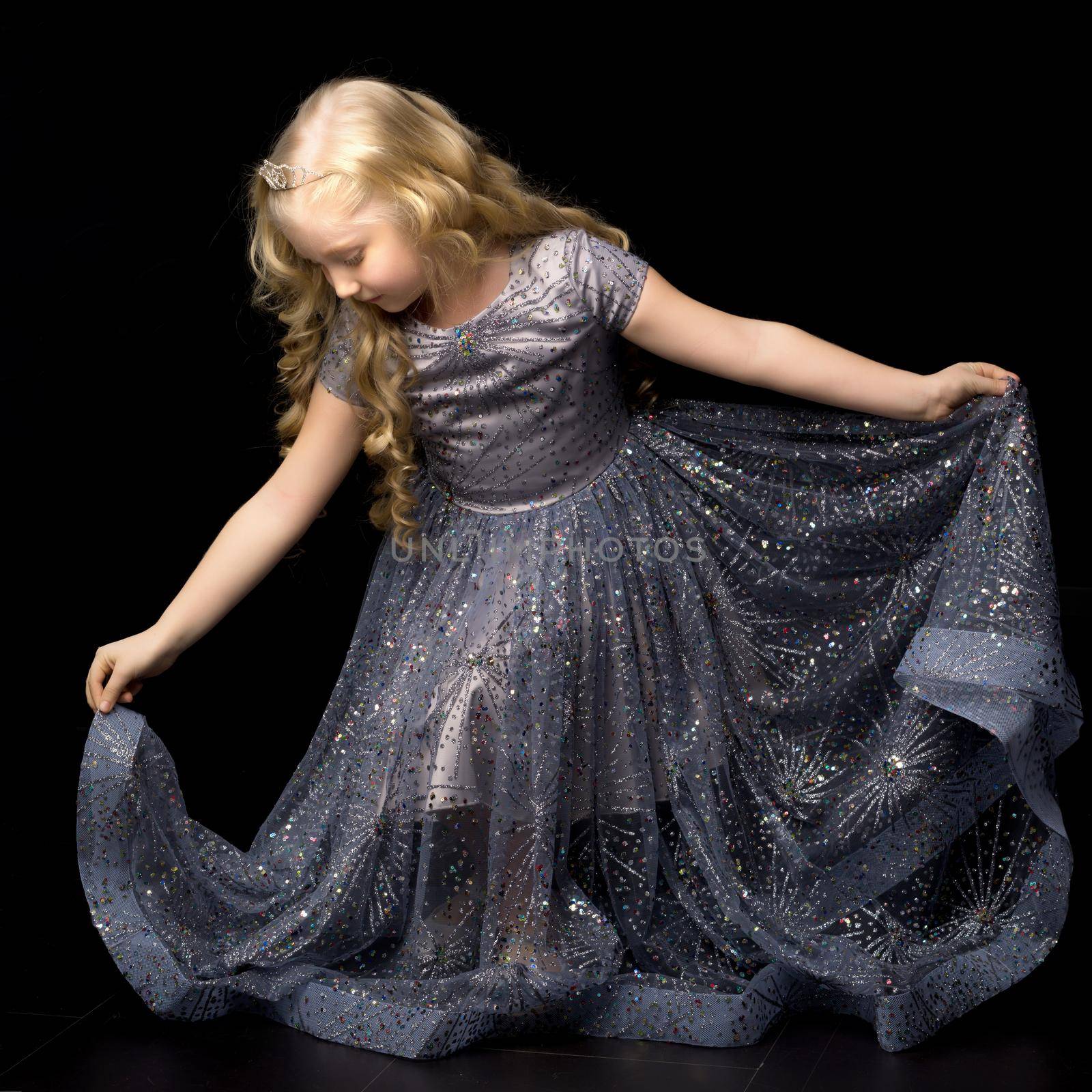 Beautiful little girl in a long, elegant dress. Studio Princess on a black background. Concepts and trendy form for a magazine cover.