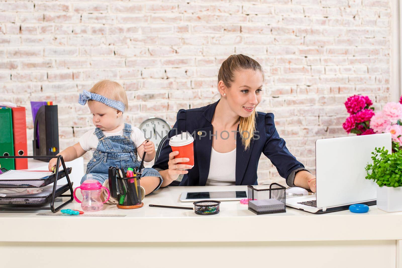 Mom and businesswoman working with laptop computer at home and playing with her baby girl. Horizontal shape, front view, waist up