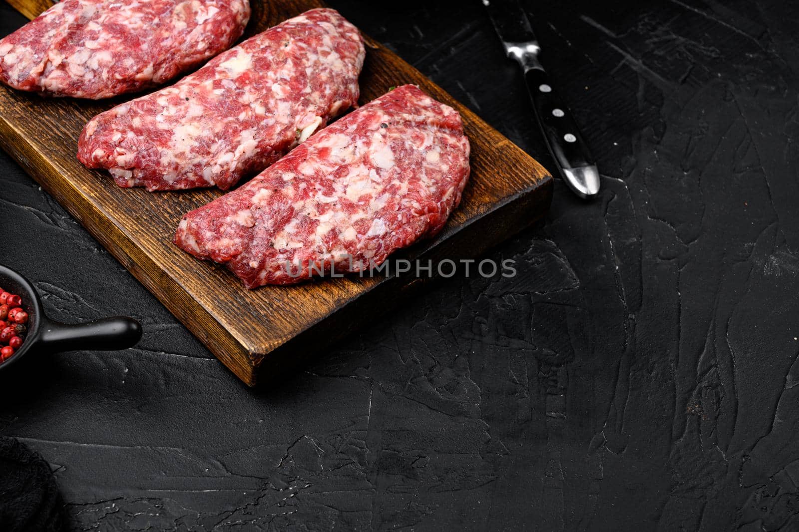 Raw beef patty set, on black dark stone table background, with copy space for text