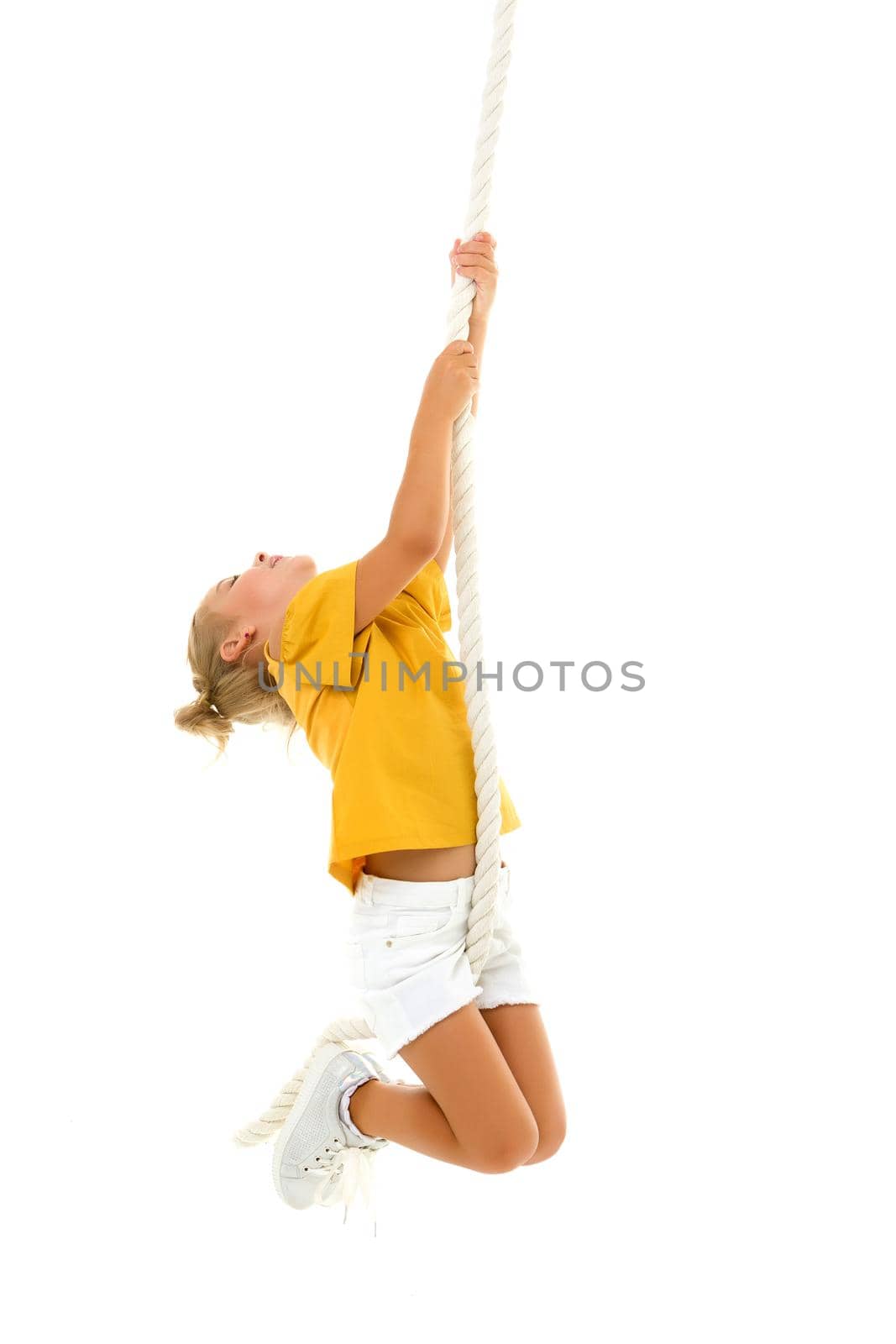 Cheerful little girl holding a rope with her hands. She tries to swing from side to side on it. Sport, fitness concept. Isolated over white background.