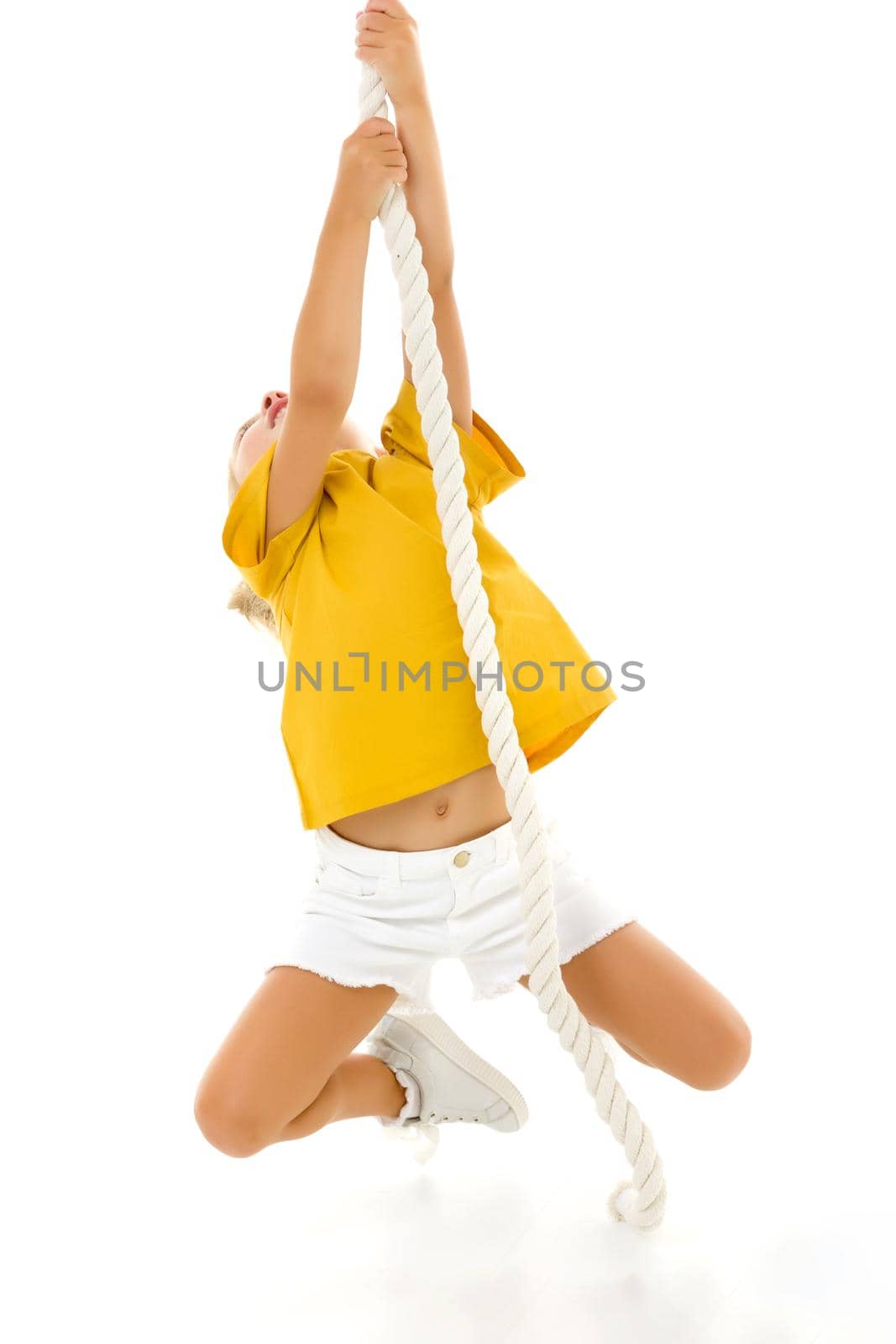 Cheerful little girl holding a rope with her hands. She tries to swing from side to side on it. Sport, fitness concept. Isolated over white background.