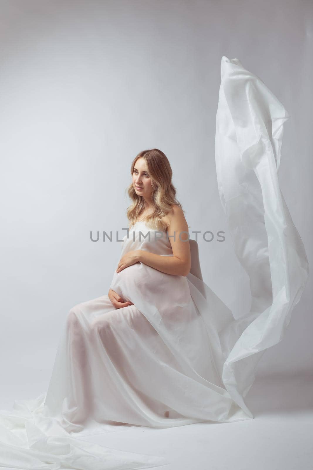 Elegant pregnant young woman standing wearing flying white fabric. Pregnancy, maternity and motherhood.