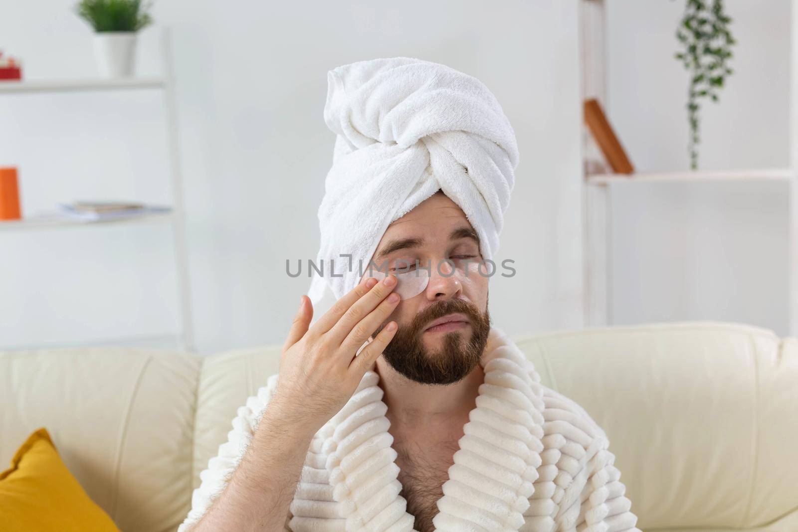 Bearded man applying eye patches on his face. Wrinkles and face home care for men