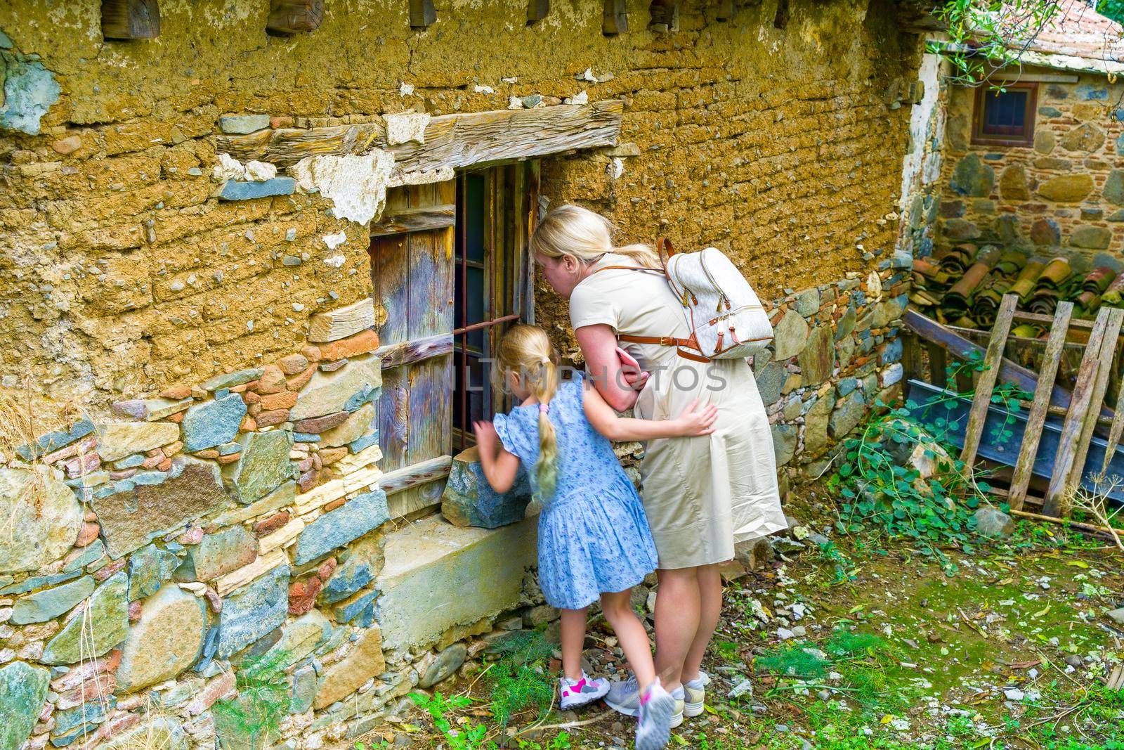 Mom and little daughter look with interest into the window of the old house.Ancient Stone Wall Made of Natural Rough Stones, Old Masonry with Cement.
