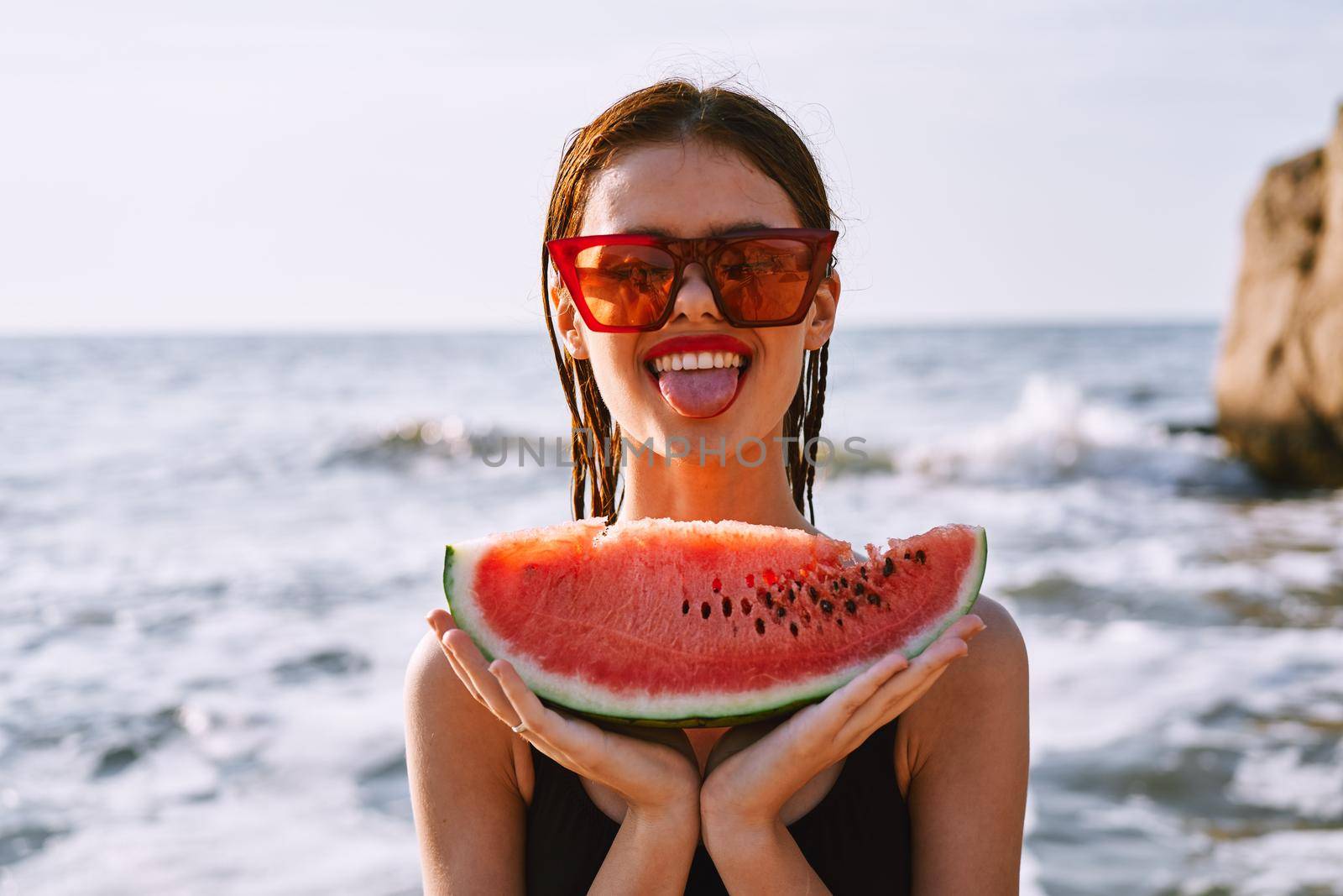 cheerful woman in sunglasses eating watermelon by the ocean. High quality photo