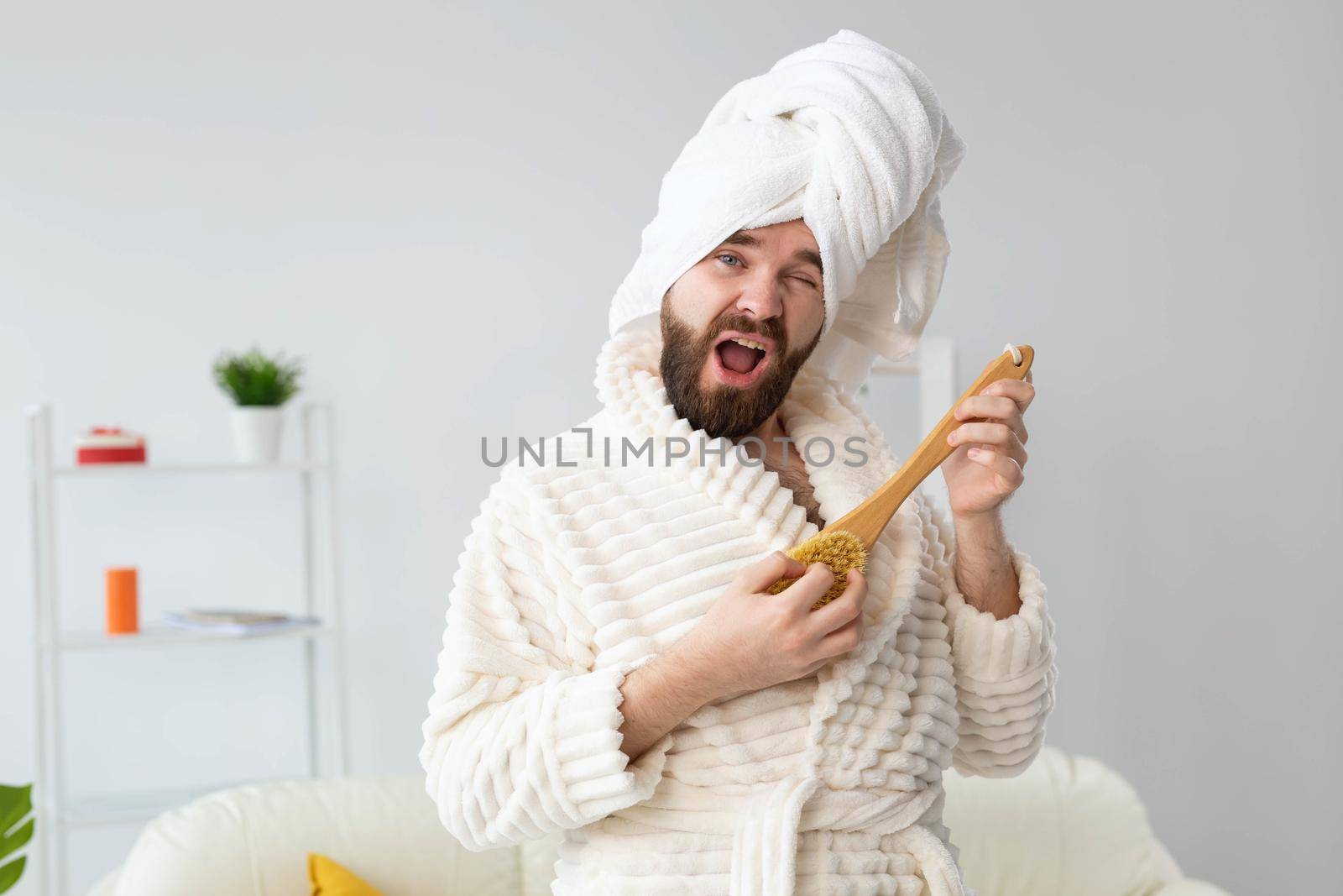 Funny handsome man pretends to play on massage brush as a guitar. Fun, spa and humor concept