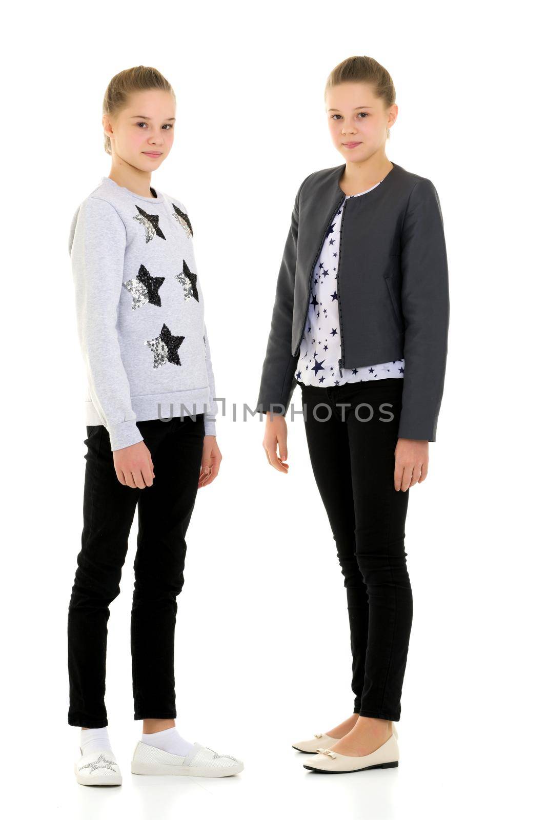 Full Length Portrait of Cheerful Pretty Sisters Standing and Looking at Camera, Two Happy Teen Girls Best Friends Wearing Trendy Stylish Clothes Posing Together in Studio Against White Background