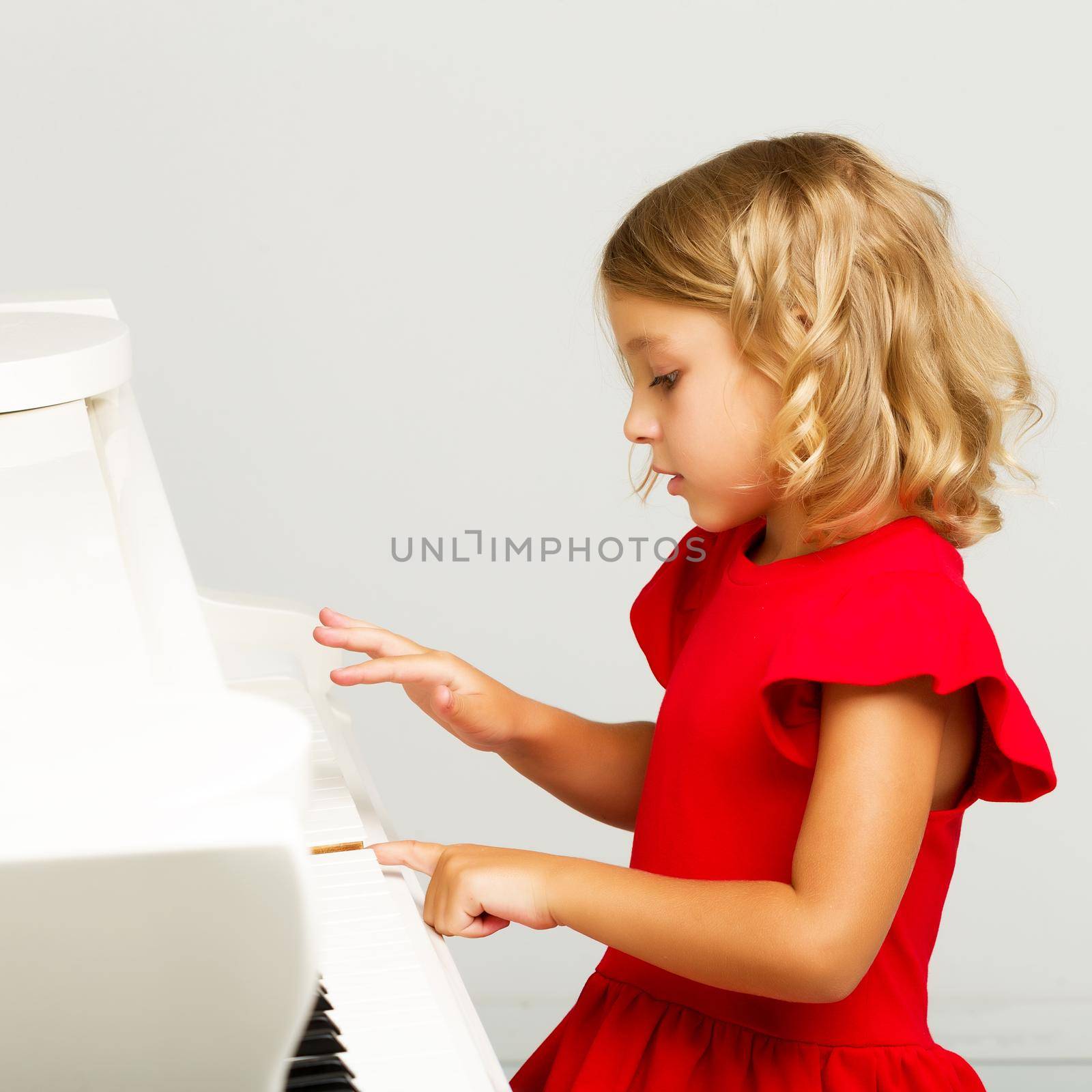 A nice little girl is playing on a big white piano. The concept of musical and aesthetic education of a child.