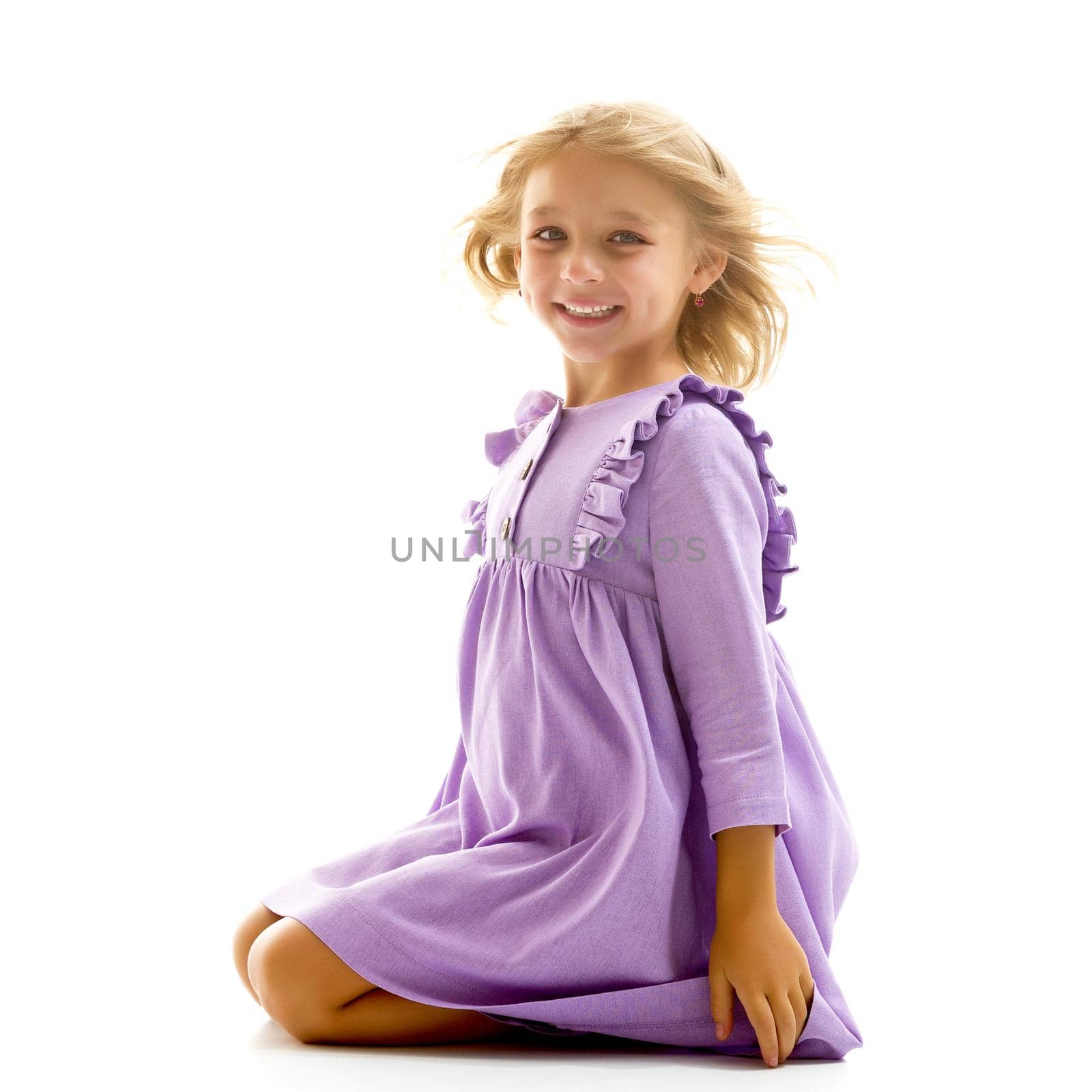 Beautiful girl sitting on the floor on her knees, thoughtful child wearing a summer dress, portrait of an adorable long-haired girl isolated on a white background