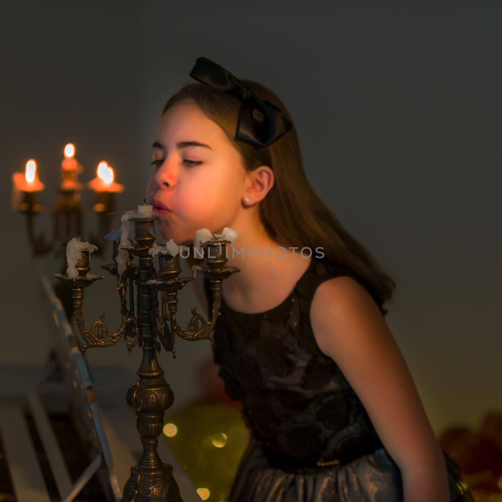 Beautiful Blonde Long Haired Girl Blowing out Candles in Vintage Chandelier, Side View of Charming Preteen Stylish Girl Sitting on Blurred Background Lighting by Warm Candle Light