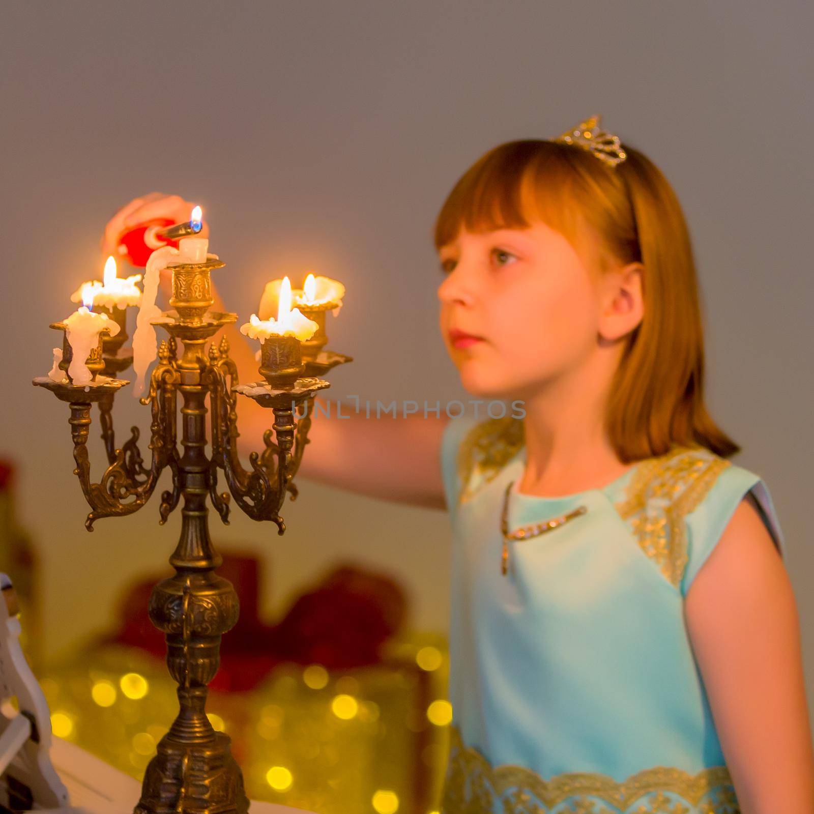 Romantic little girl lights candles on Christmas night. Family holidays concept.