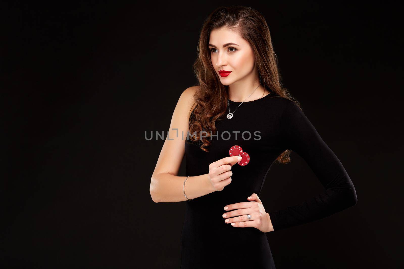 Sexy curly hair brunette in black dress posing with chips in her hands, poker concept black background. Casino, poker, Roulette Blackjack Spin.