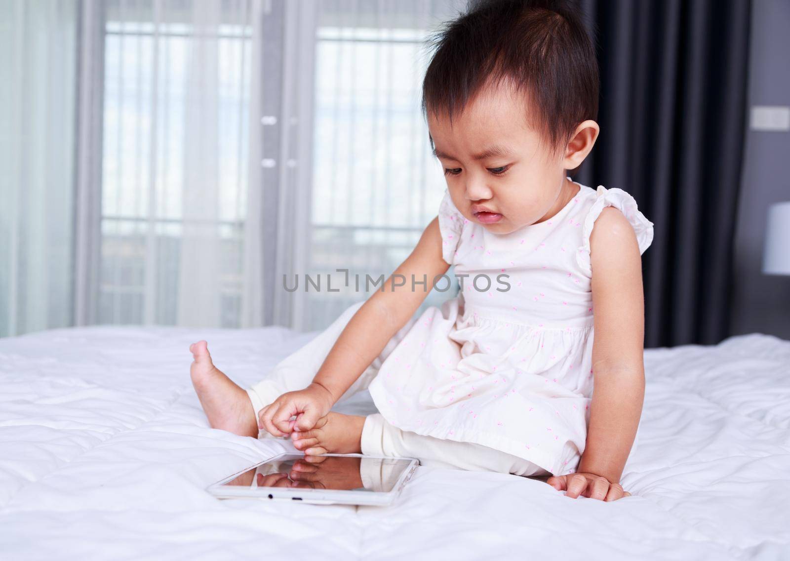 baby are looking to play and read tablet computer on bed  by geargodz