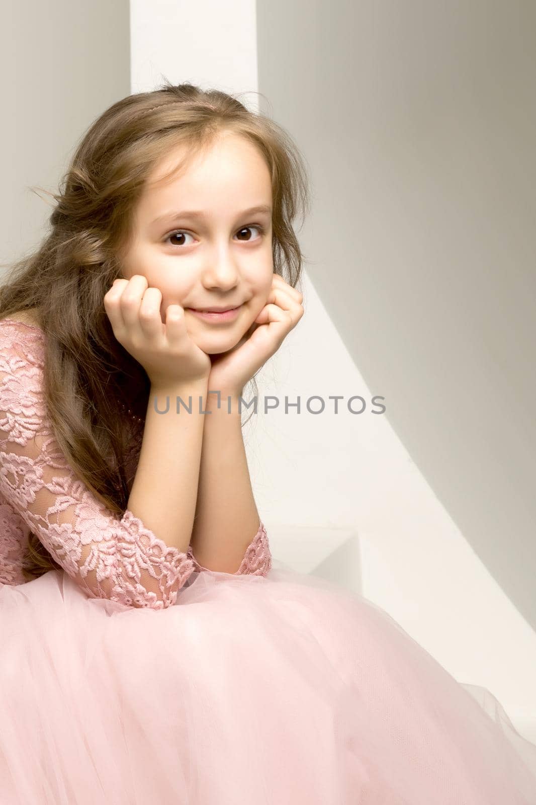 Beautiful little girl posing in the studio. She folded her arms near her face, and looks directly at the camera.Children's emotions concept. Close-up.