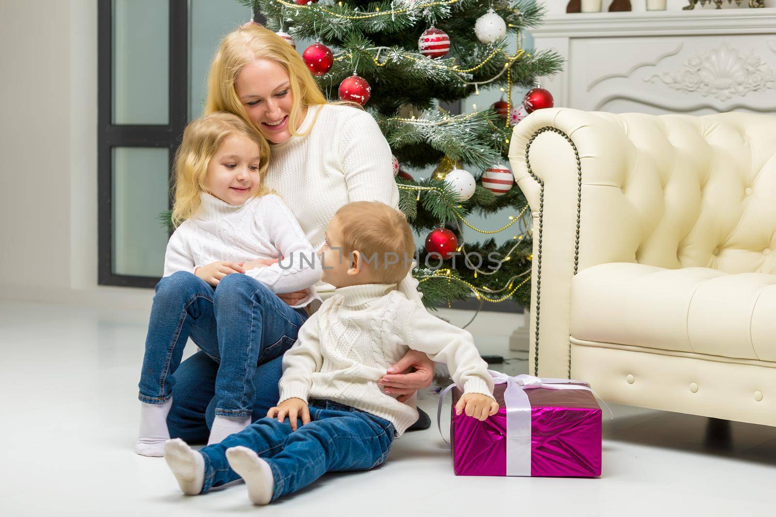 Cheerful Mom Hugging her Cute Little Kids while Sitting on the Floor in Front of Decorated Christmas Tree, Happy Family Having Fun Celebrating Xmas and New Year, Winter Holidays
