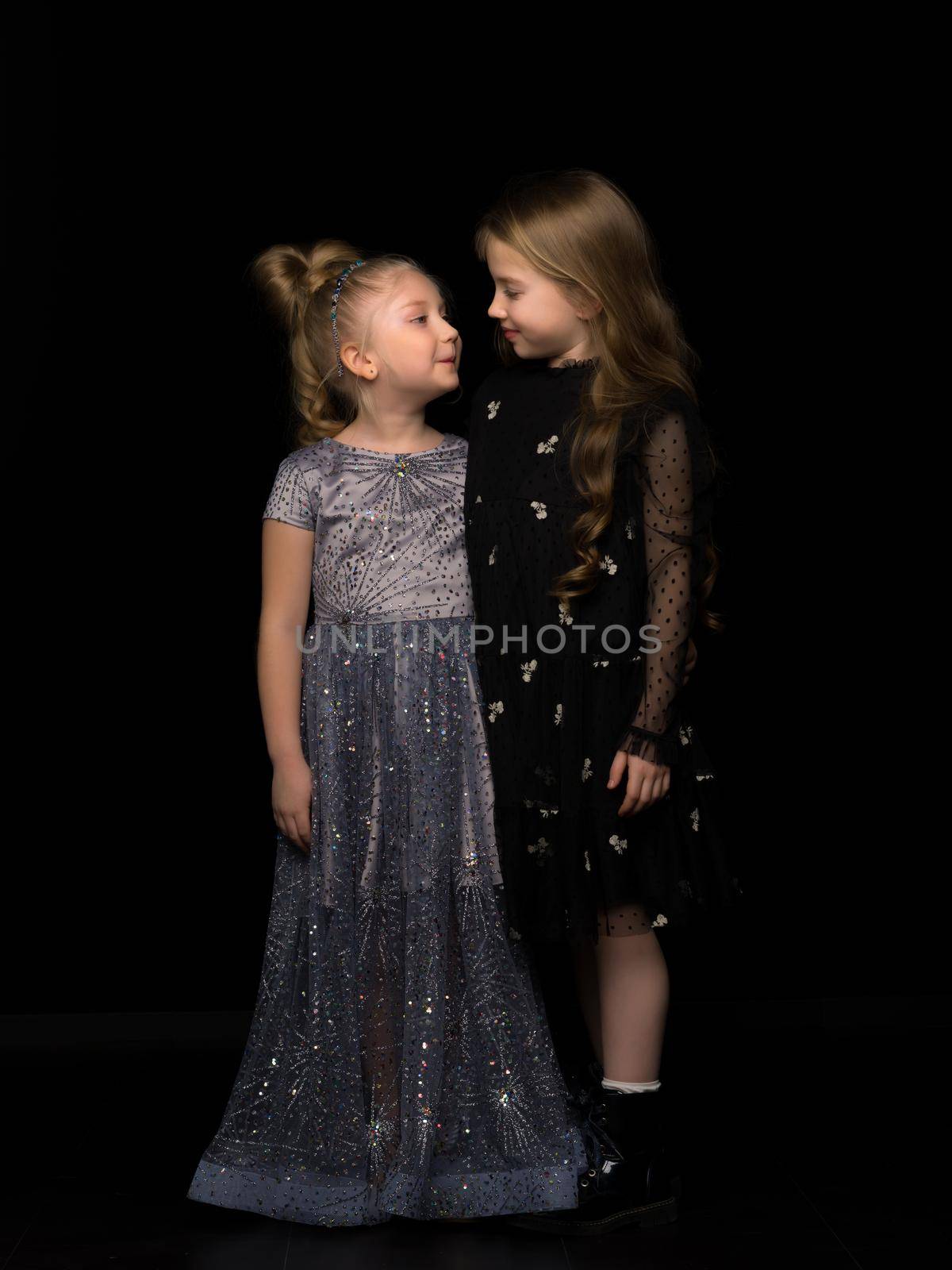 Two little girls posing in the studio on a black background. Style and fashion concept. by kolesnikov_studio