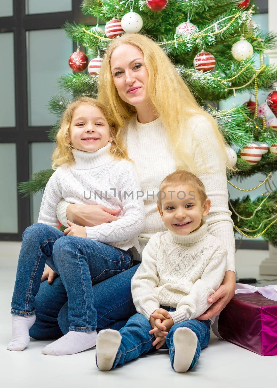 Cheerful Mom and her Cute Daughter and Son Sitting Next Christmas Tree. by kolesnikov_studio
