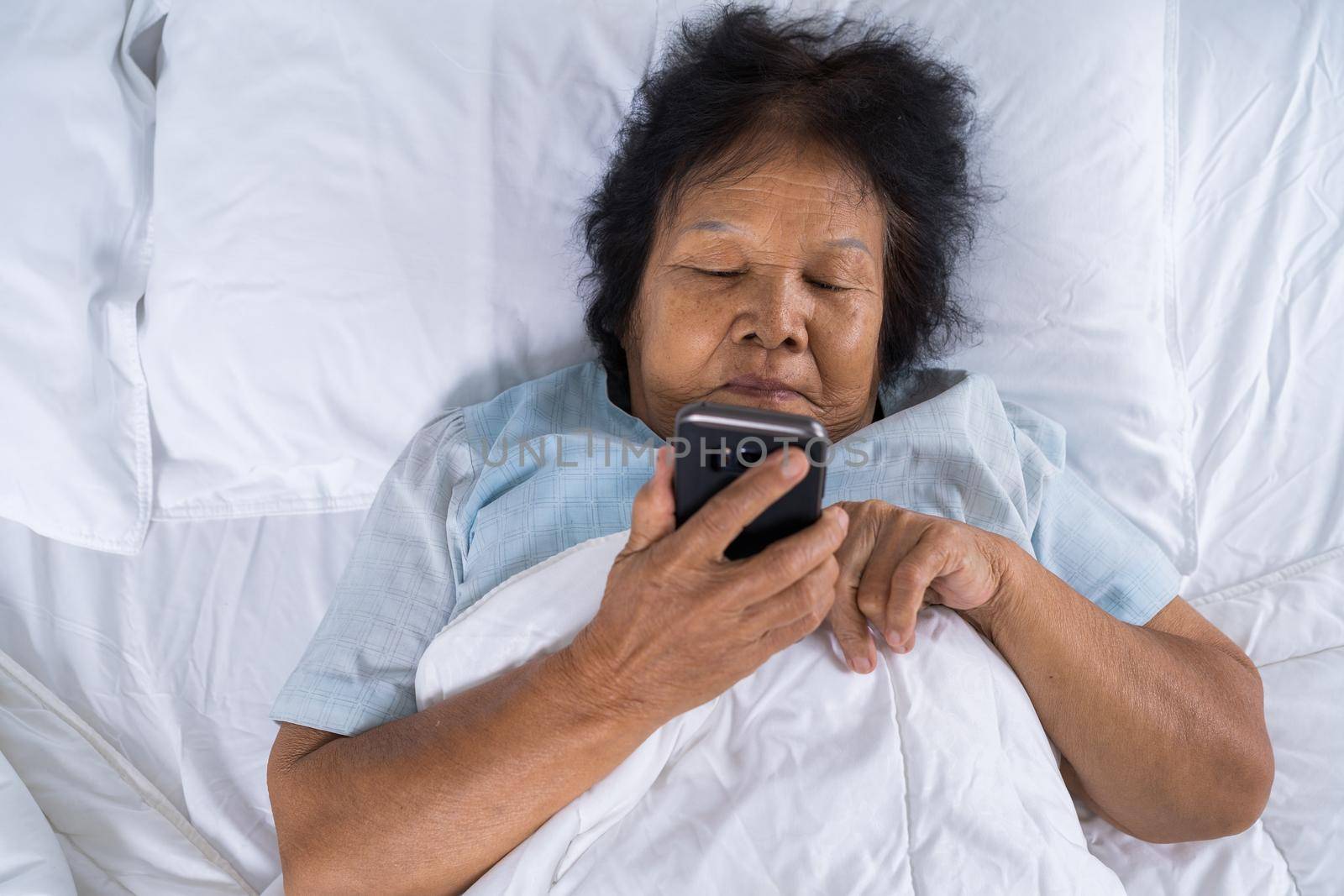 senior woman using mobile phone on bed by geargodz