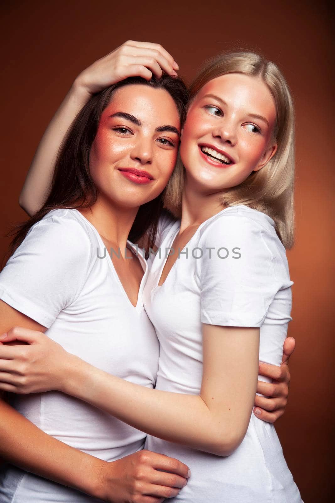 wo pretty diverse girls happy posing together: blond and brunette on brown background, lifestyle people concept by JordanJ