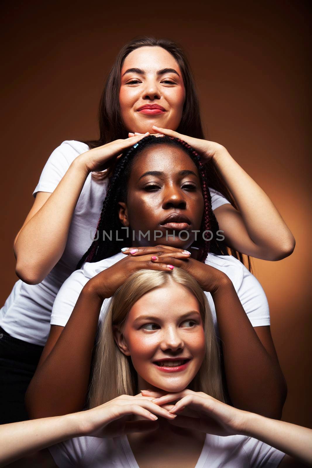 young pretty asian, caucasian, afro woman posing cheerful together on brown background, lifestyle diverse nationality people concept closeup
