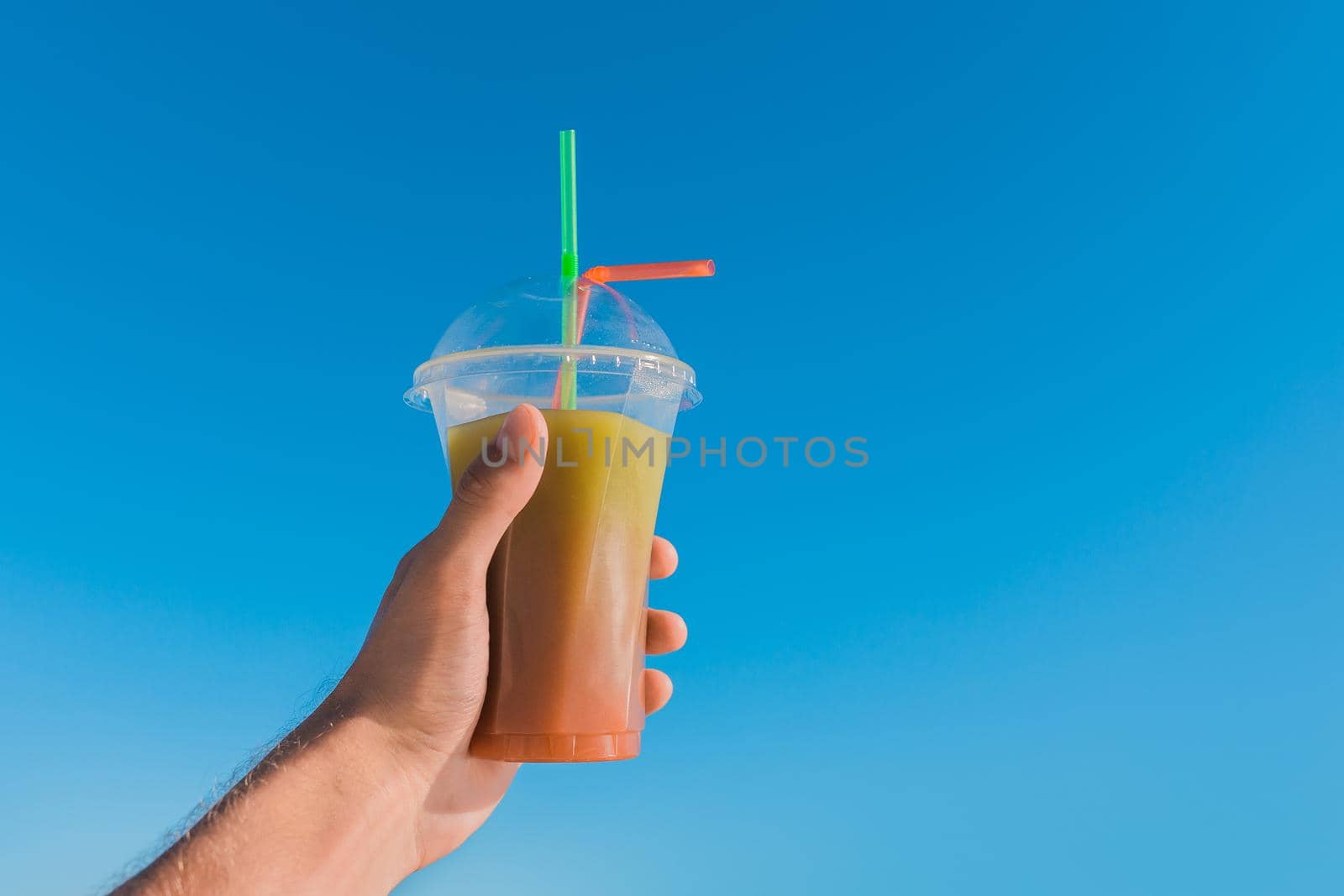 The guy's hand holds a colored chilled non-alcoholic cocktail against the background of the blue sky.