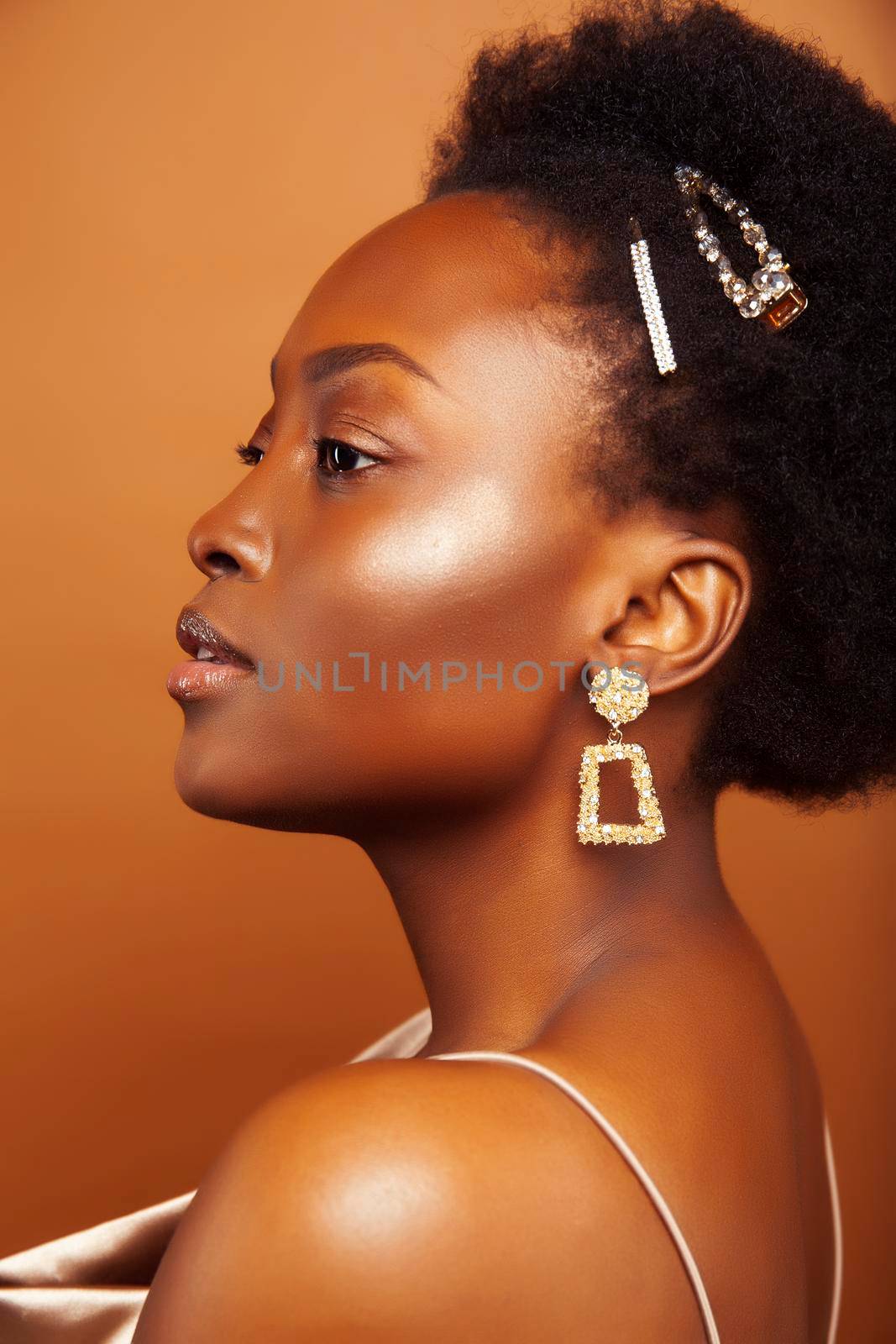 young pretty african model with golden jewelry in fashion style dress smiling happy on brown backround, lifestyle people concept by JordanJ