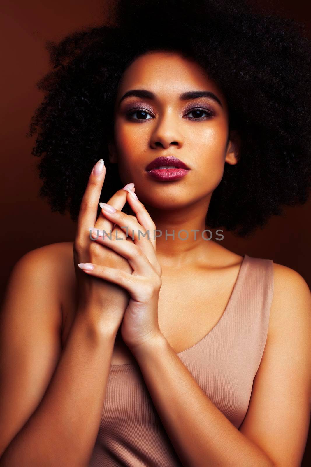 pretty young african american woman with curly hair posing cheerful gesturing on brown background, lifestyle people concept closeup
