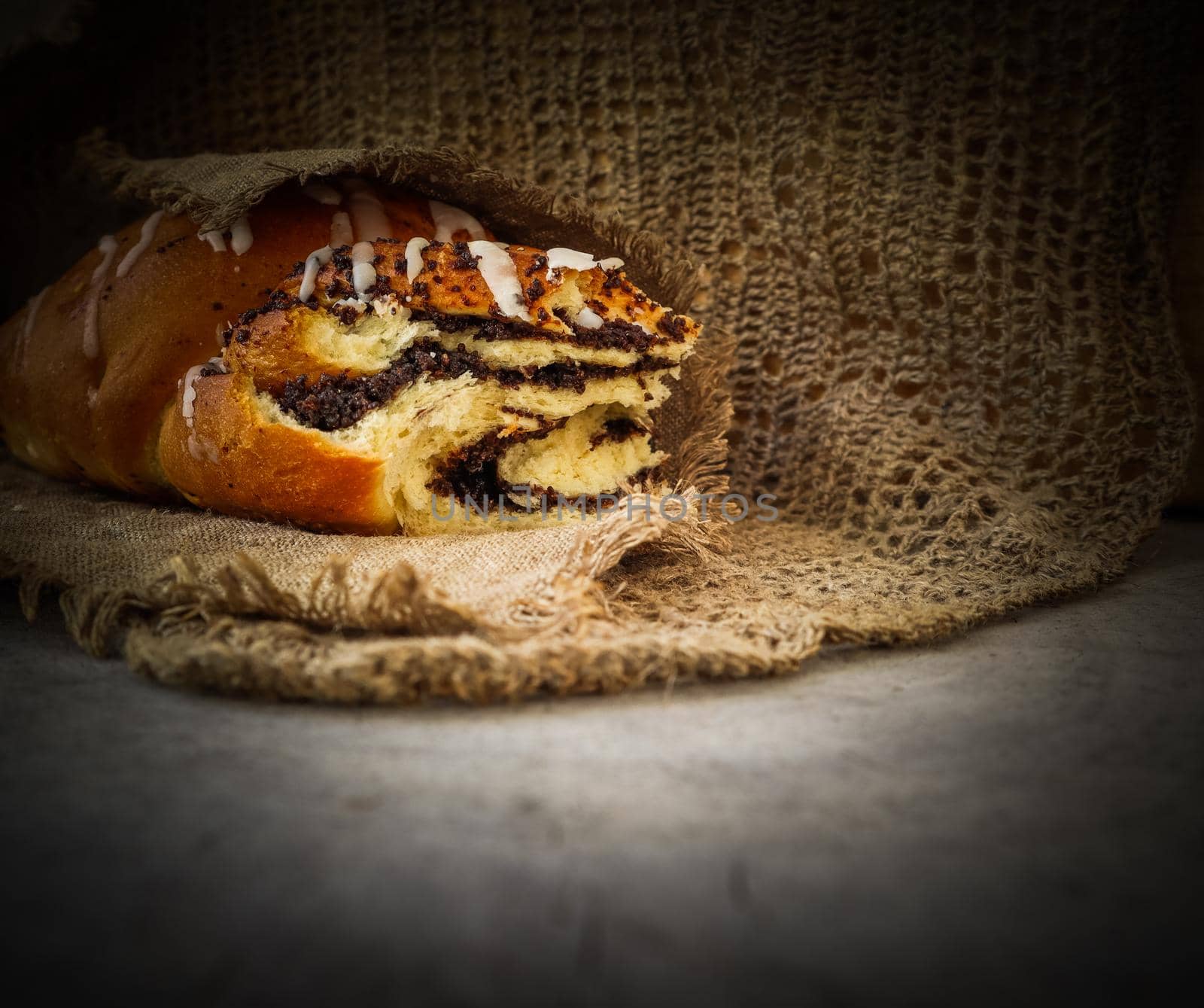 Fresh poppy seed roll on natural linen napkin on rustic wooden background