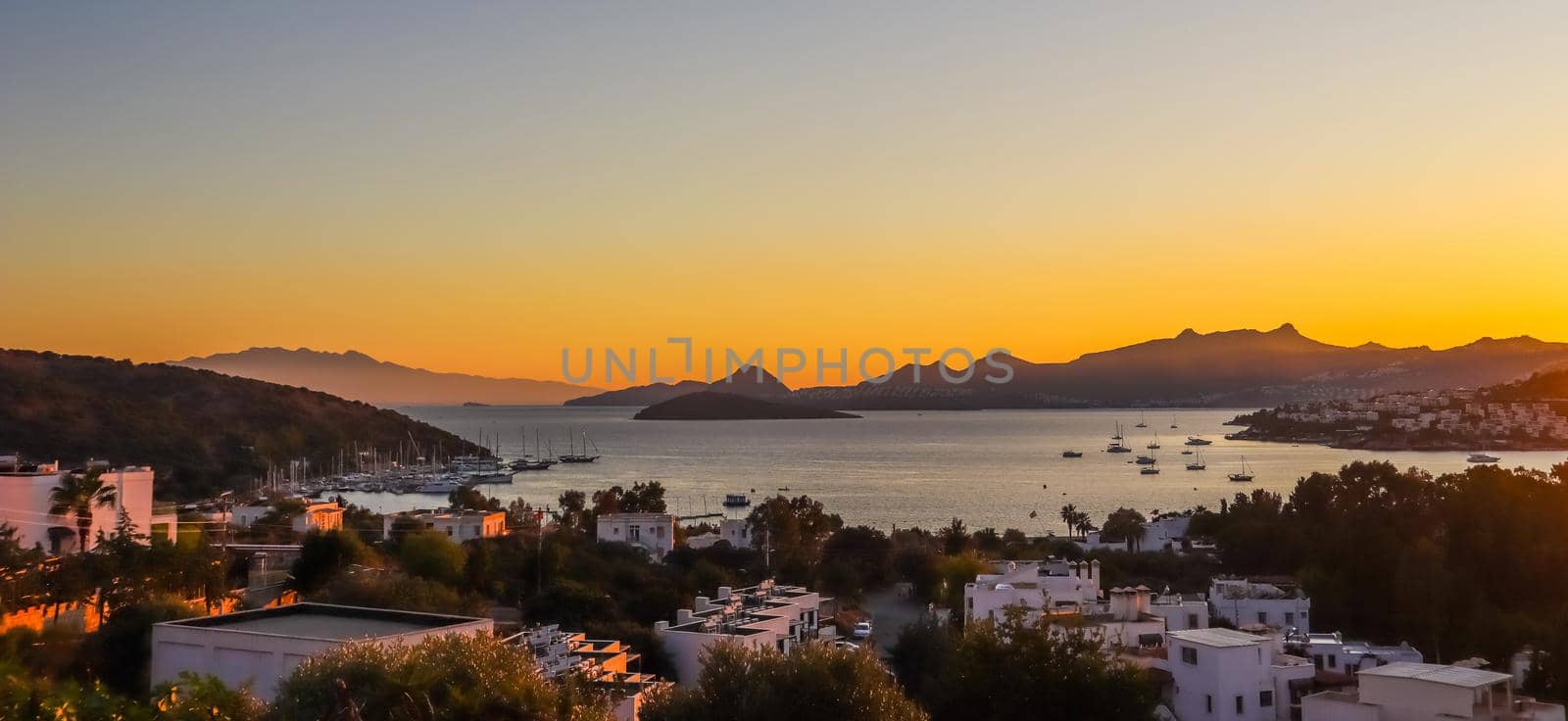 Bright colorful sunset in the beautiful bay of the Aegean sea with islands, mountains and boats. Summer holiday concept and travel background