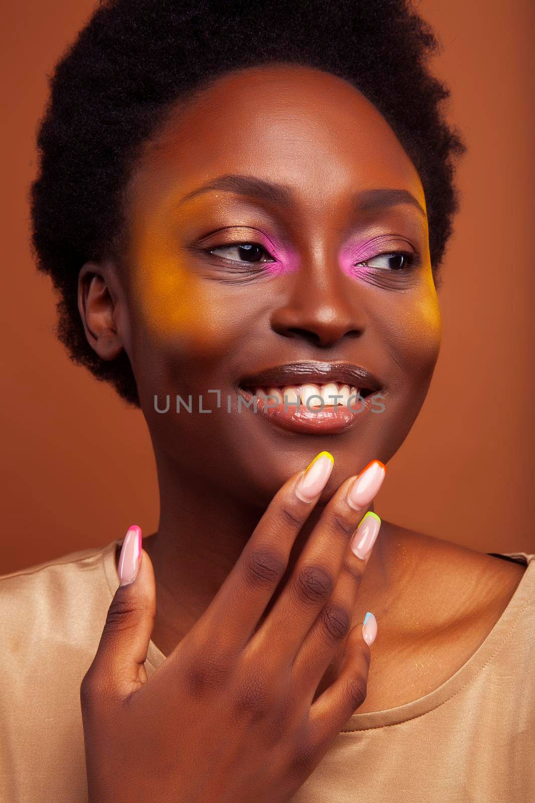 pretty young african american woman with curly hair posing cheerful gesturing on brown background, lifestyle people concept by JordanJ