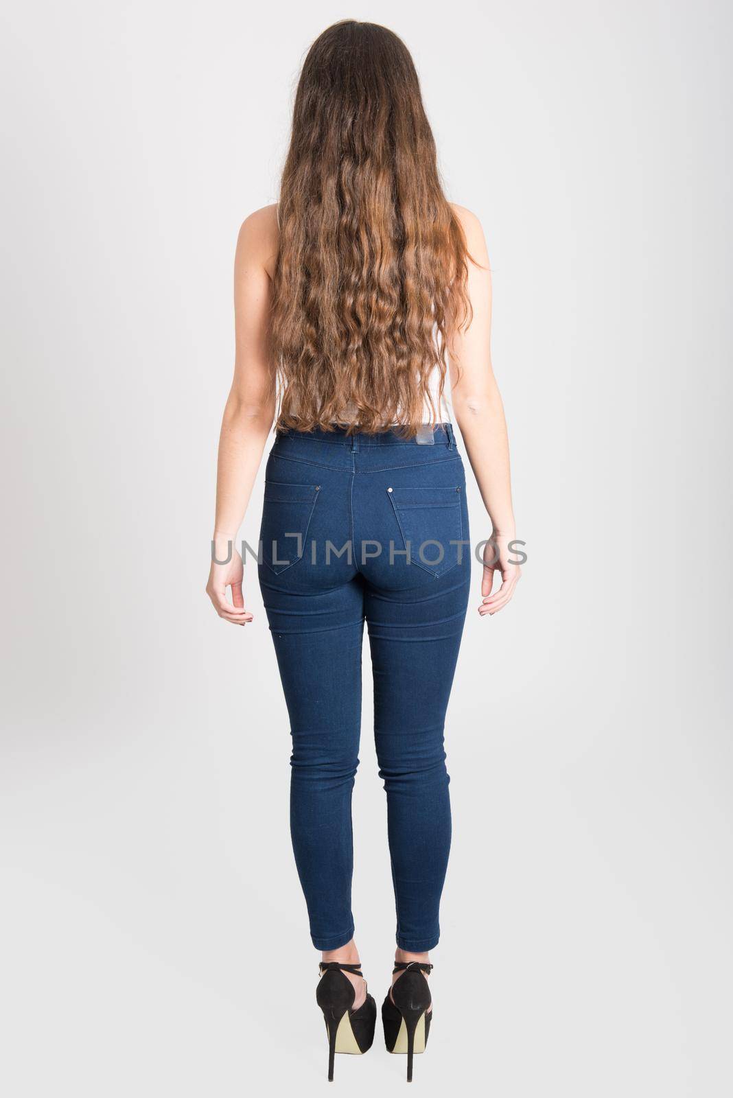 Back view of young woman with long hair wearing white t-shirt and blue jeans on white background