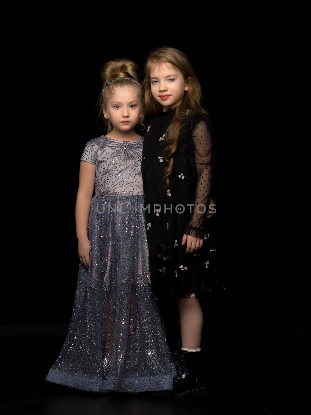 Two little girls posing in the studio on a black background. Style and fashion concept. by kolesnikov_studio