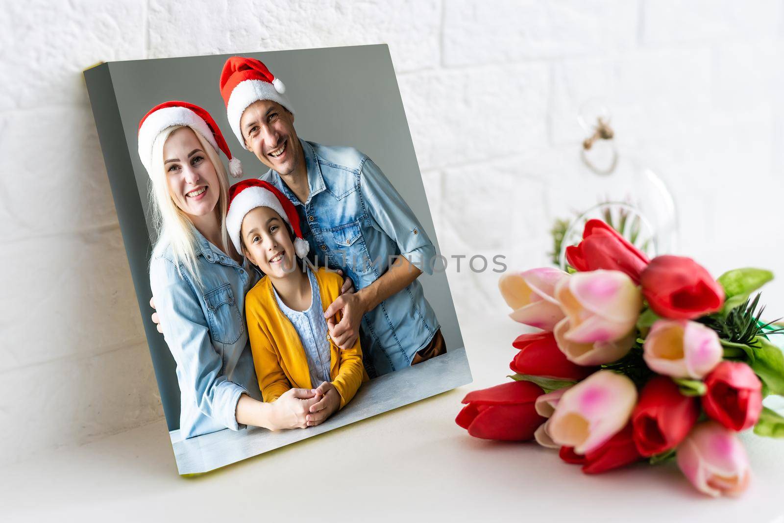 Photo printed on canvas, white background. Happy young family in Santa hats celebrating Christmas at home.