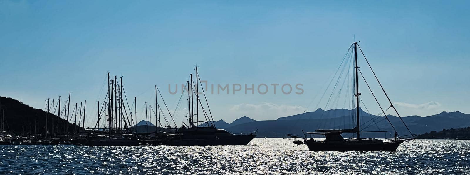 Tranquil seascape and coastal nature concept. Sea, boats, mountains and blue sky over horizon at sunset.