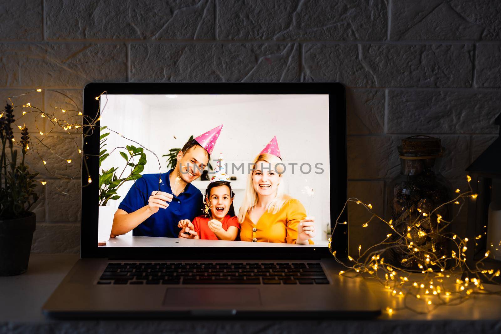 Happy parents hugging cute small kid daughter holding present giving Christmas gift to web camera during virtual family social meeting on video conference call party at home, laptop webcam view