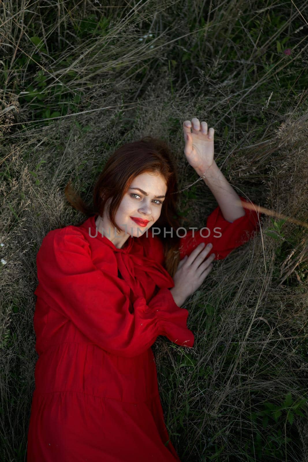 pretty woman in red dress lies on the grass posing top view. High quality photo