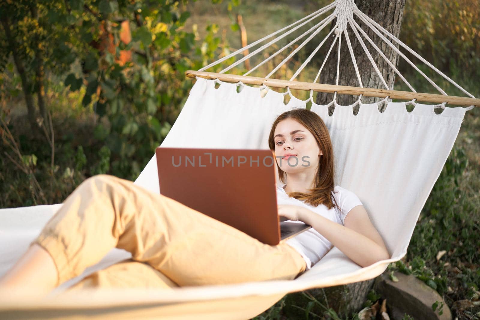 woman outdoors with laptop lies in hammock leisure technology. High quality photo